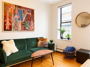 Ein Zimmer mit einem grünen Sofa, einem runden Spiegel, einem Holztisch und einem großen abstrakten Gemälde.