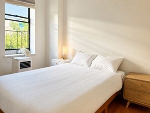 Ein Schlafzimmer mit Bett, Nachttisch, Lampe, Klimaanlage und Fenster mit Blick.