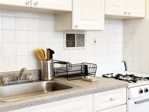 Eine Küche mit weißen Schränken, einer Edelstahl-Spüle, einem Gasherd und einem schwarzen Drahtgestell.
