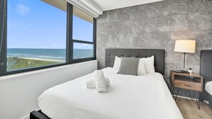 Habitación de hotel con cama, mesita de noche, lámpara y vista al océano.