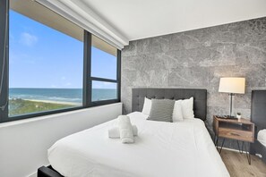 Ein Hotelzimmer mit Bett, Nachttisch, Lampe und Meerblick.