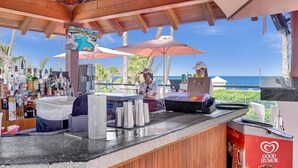 Zona de bar con mostrador de madera, una persona atendiendo y vista al océano.