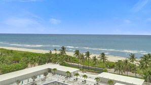 Un hotel con piscina en la azotea, palmeras y vistas a la playa y el océano.