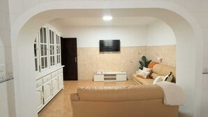 Ein Zimmer mit einem beigefarbenen Sofa, einem an der Wand befestigten Fernseher und einer Uhr über dem Sofa.