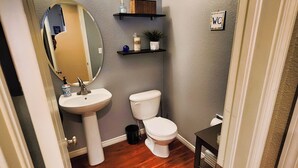 Une salle de bain avec un lavabo blanc, des toilettes, un miroir et une étagère ornée d’objets décoratifs.