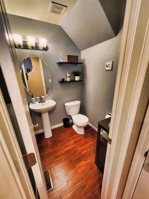 A bathroom with a white sink, a toilet, a mirror, and a shelf with decorative items. - Broadmoor Retreat Mtn Views Hiking and Biking (Colorado Springs)