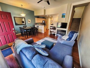 A living room with a sofa, a dining table with chairs, a kitchen area, a fireplace, and a TV mounted on the wall. - Broadmoor Retreat Mtn Views Hiking and Biking (Colorado Springs)