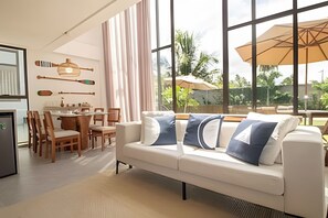 A modern living room with a white sofa, dining table, and chairs. - Oka Milagres Cond. Beira Mar By MME (Passo de Camaragibe)