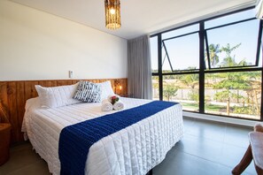 Een slaapkamer met een groot bed, een houten hoofdbord, uitzicht op de natuur en een plafondlamp.