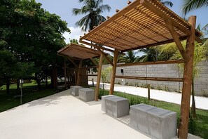 Uma área de estar coberta ao ar livre, com bancos de concreto e um muro de pedra ao fundo.