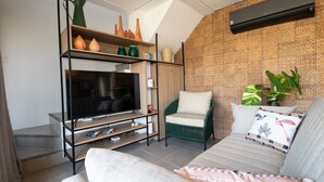 A living room with a TV, sofa, green chair, and patterned wall. - Oka Milagres Cond. Beira Mar By MME (Passo de Camaragibe)