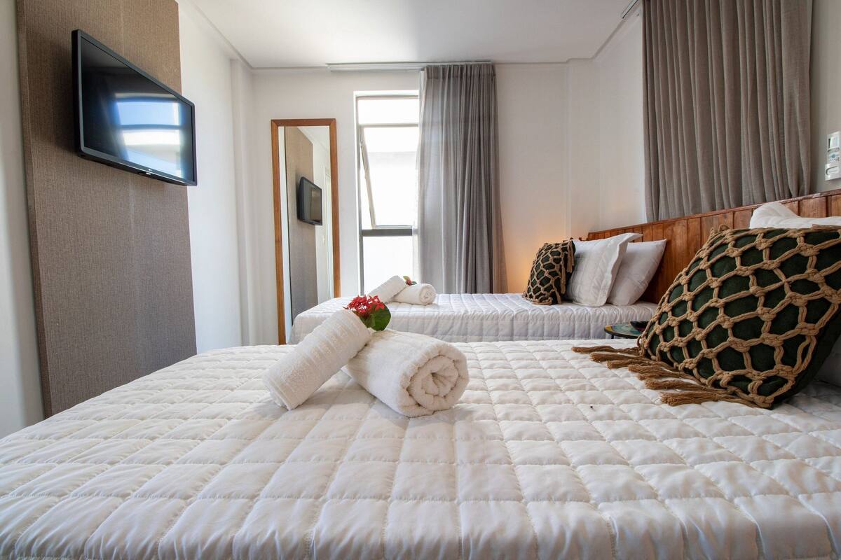Quarto de hotel com duas camas, uma televisão de tela plana na parede, uma janela com cortinas e um espelho.