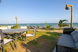 Een terras aan het strand met een tafel, stoelen en een bank, met uitzicht op zee.