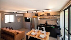 A modern kitchen with a dining area, a sofa, and a TV mounted on the wall. - Oka Milagres Cond. Beira Mar By MME (Passo de Camaragibe)