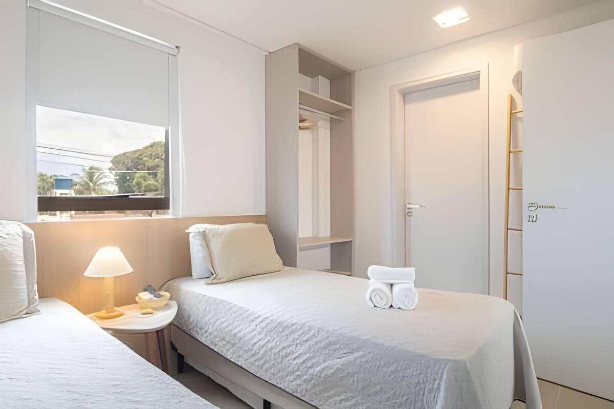 Quarto de hotel com duas camas, uma mesa de cabeceira com abajur, banheiro com espelho e vista para o exterior.