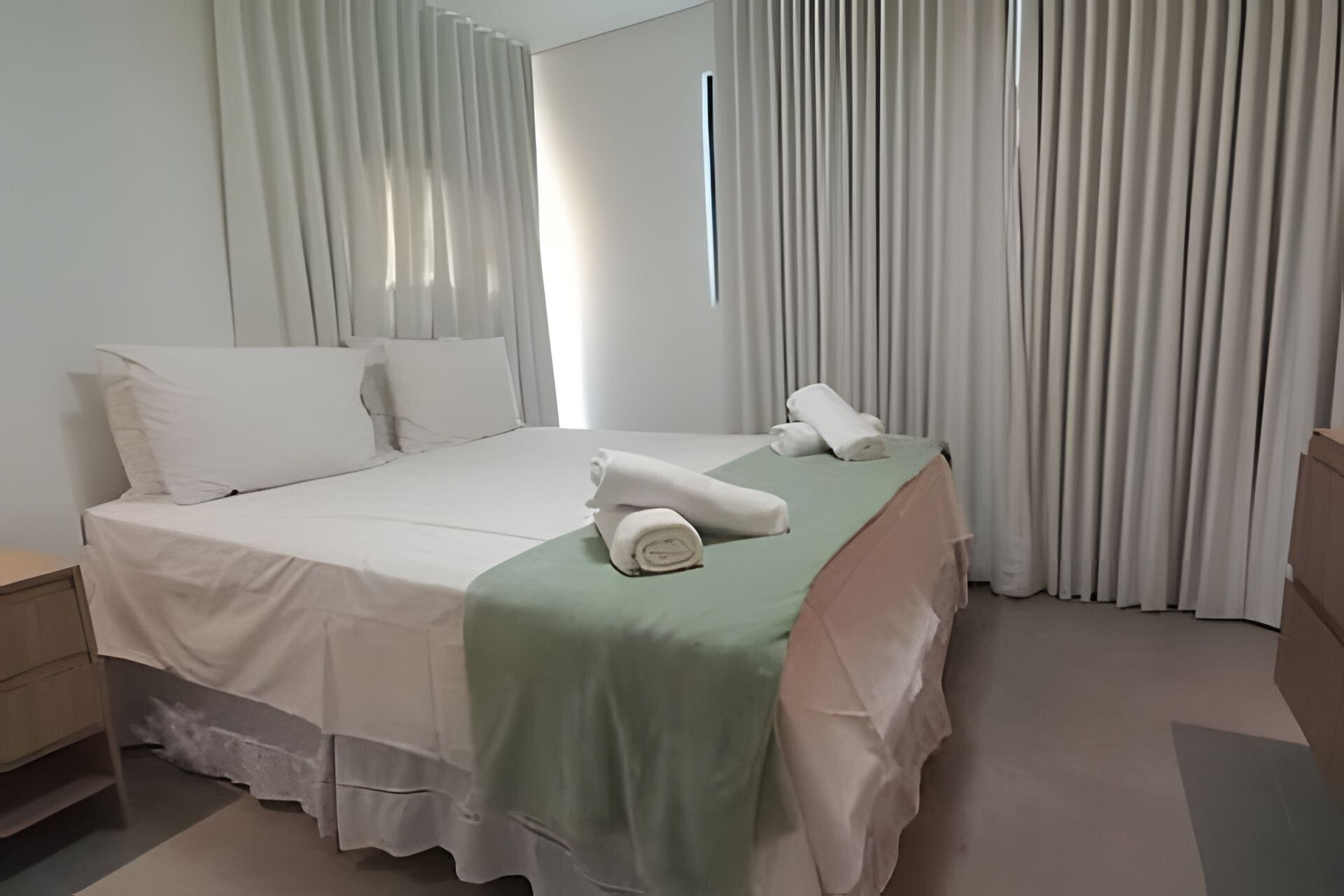 Une chambre d’hôtel avec un lit, des oreillers, une couverture verte et une serviette enroulée.