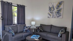Uma sala de estar com um sofá cinza, um banquinho a combinar e uma luminária.