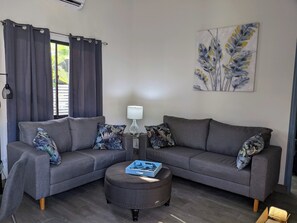 Un salon avec un canapé gris, un pouf assorti et une lampe.