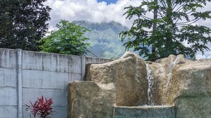 Uma pessoa relaxa perto de uma piscina com cascata, um vaso de planta e uma bebida sobre uma mesa.