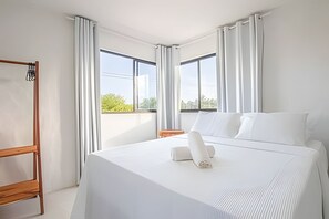 Ein Hotelzimmer mit einem großen Bett, einem Holzstuhl und zwei mit Vorhängen versehenen Fenstern.