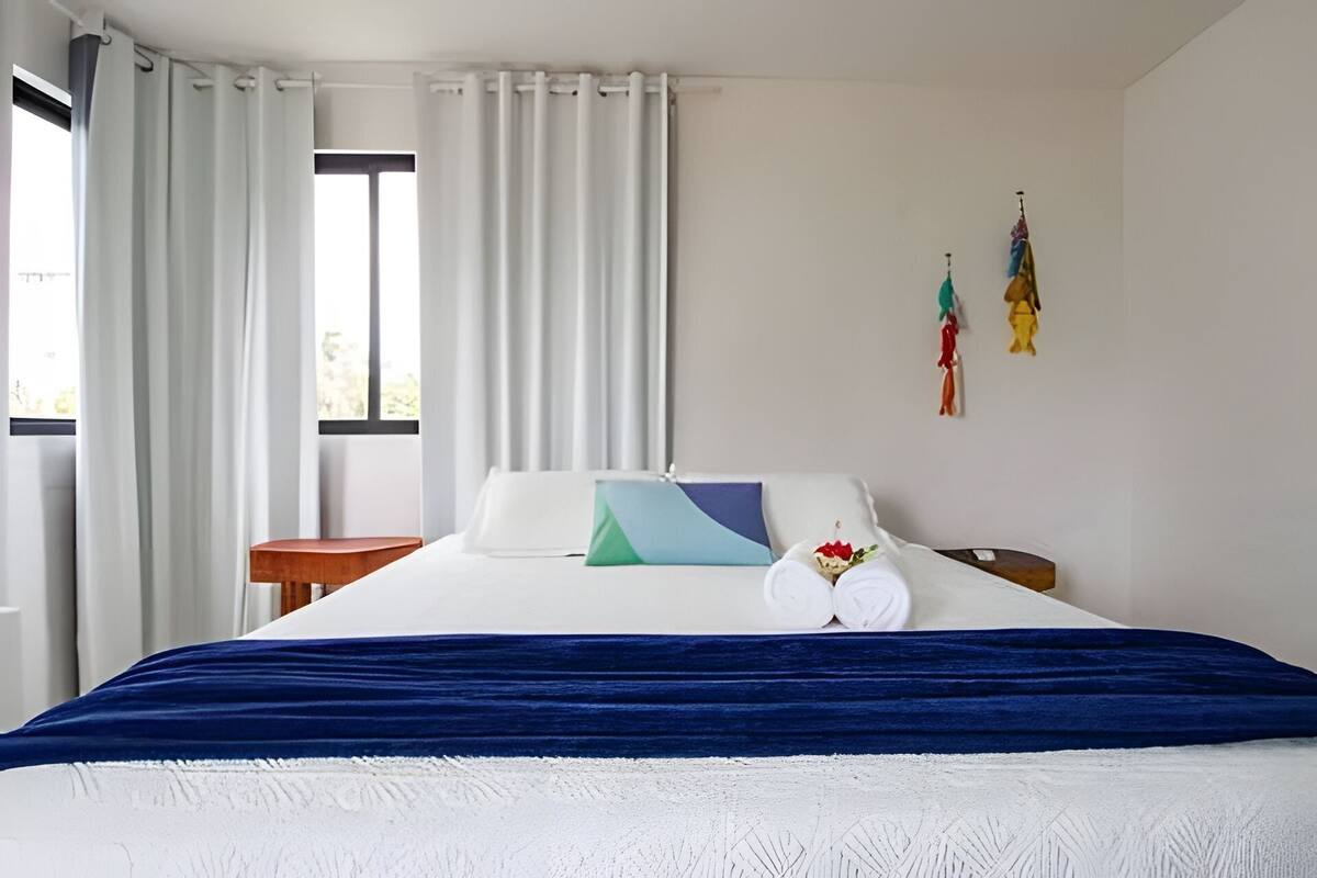 Ein Hotelzimmer mit einem Bett, weißen Vorhängen, einem kleinen Tisch und einem Fenster.