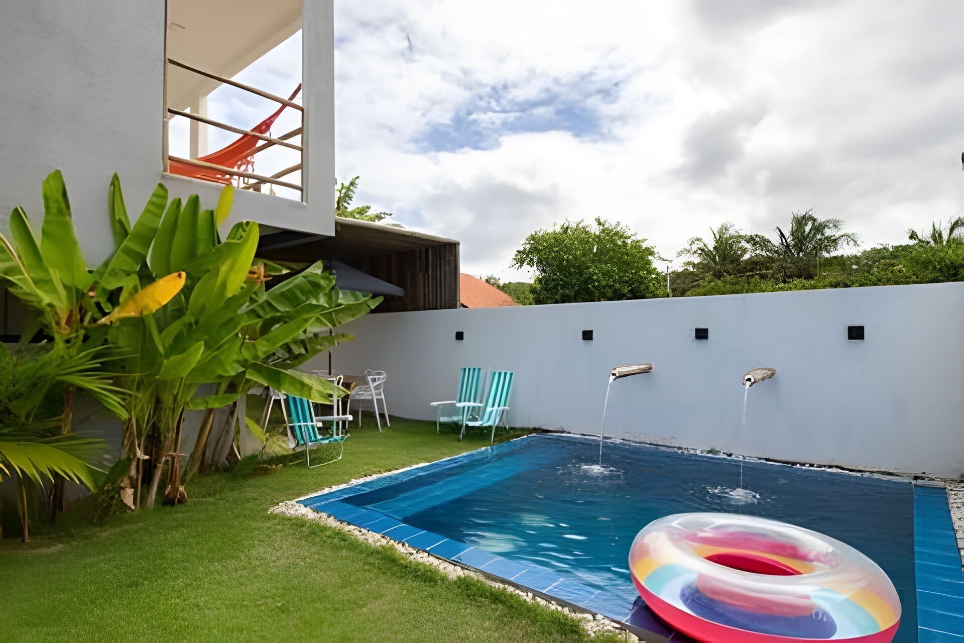 A swimming pool with a slide, green chairs, and a colorful inflatable ring.