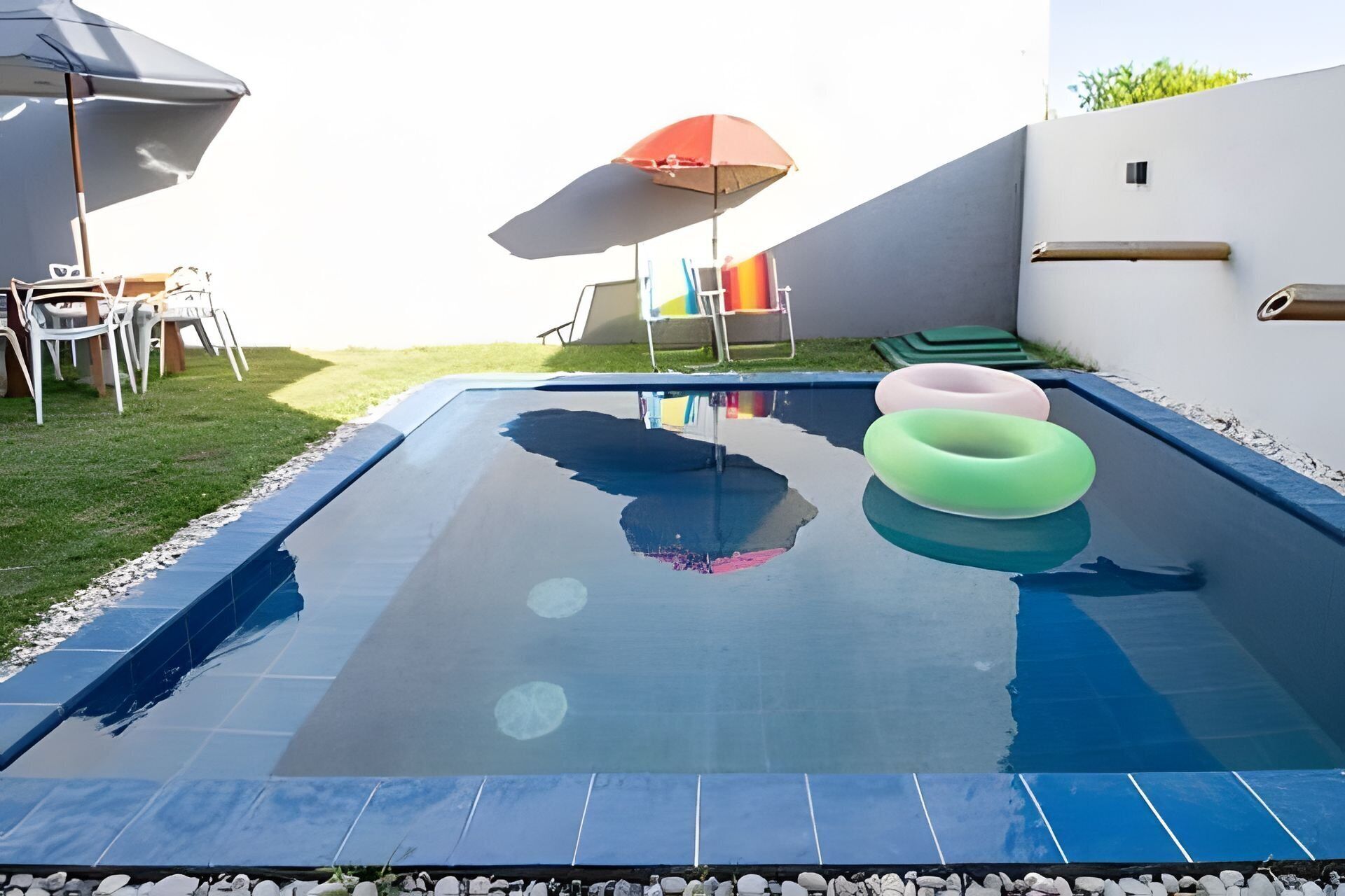 Una piscina con flotadores, una sombrilla y una silla con un cojín colorido.