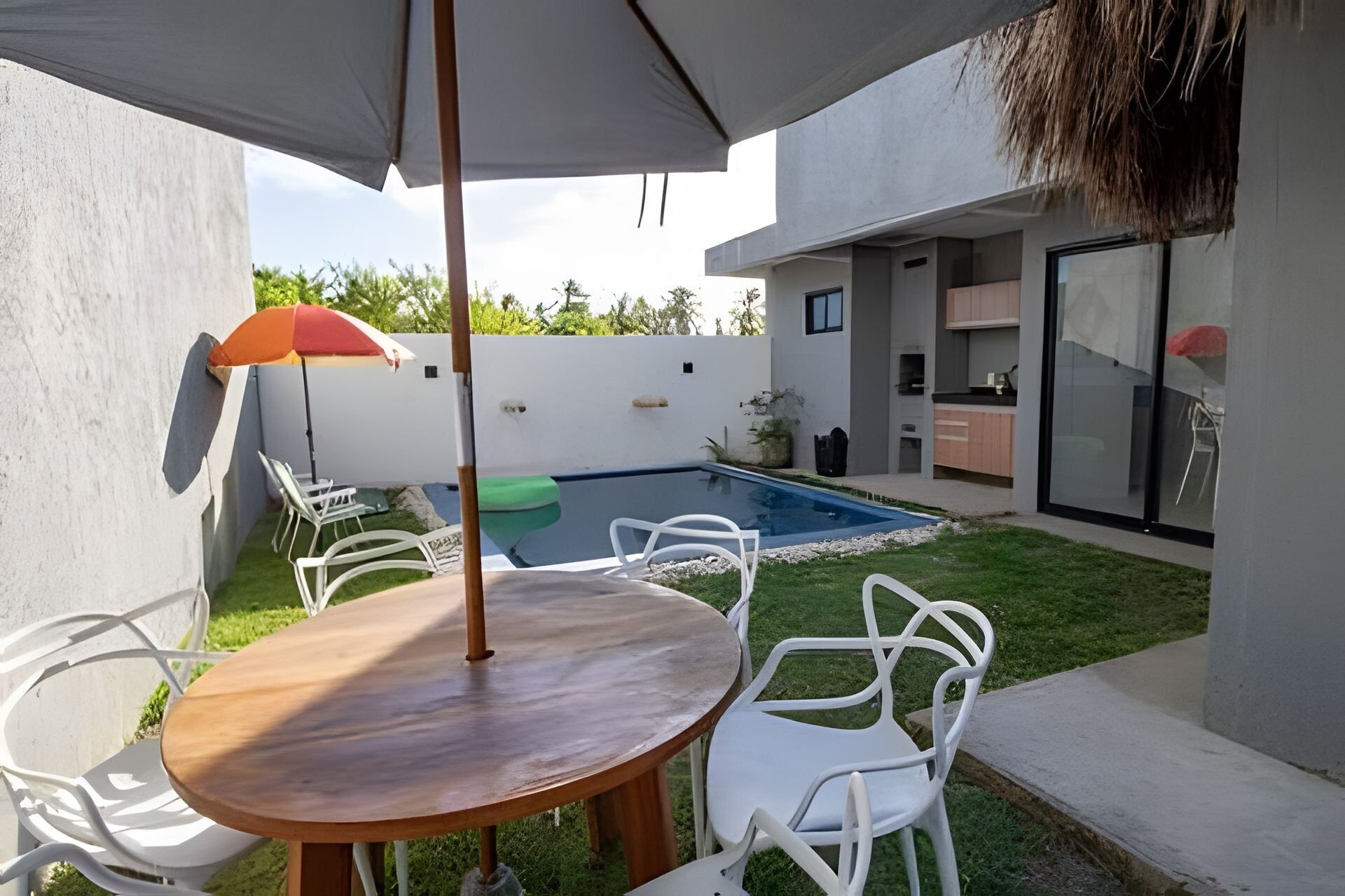 Een modern terras buiten met een zwembad, witte stoelen en een houten tafel.