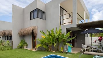 Een modern huis met een zwembad, een gebouw met rieten dak en een terras.