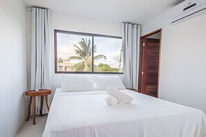 Ein Schlafzimmer mit großem Fenster, einem Bett, einem kleinen Tisch und einer Holztür.