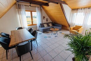 Ein Essbereich mit Holztisch und Stühlen, einem grauen Sofa, einem kleinen runden Tisch und einer Pflanze im Topf.