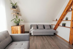 Ein Loft-Zimmer mit grauem Sofa, Holzboden und einer Holztreppe.