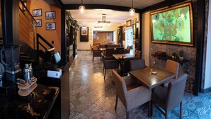 Een restaurant met een bar, eettafels, stoelen en een groot schilderij in een lijst aan de muur.