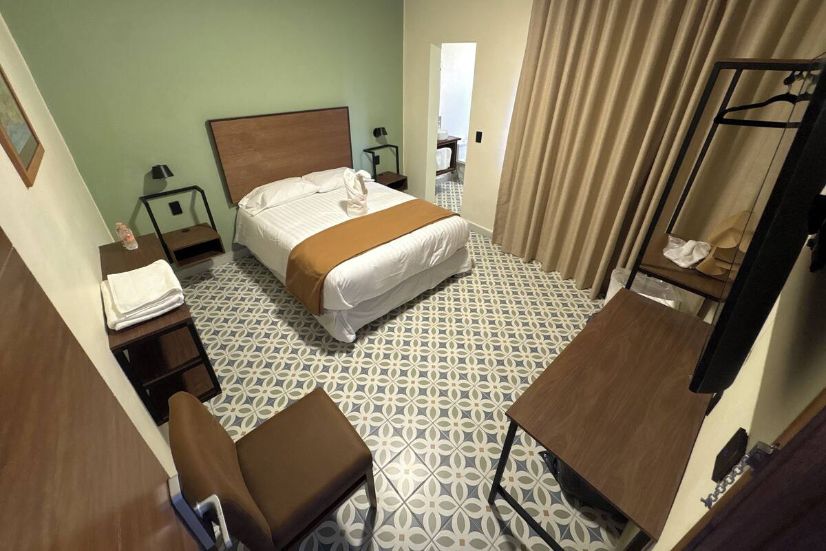 Habitación de hotel con cama, escritorio, silla, espejo y suelo estampado.