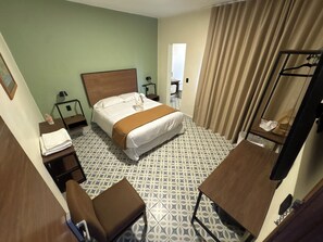 Habitación de hotel con cama, escritorio, silla, espejo y suelo estampado.