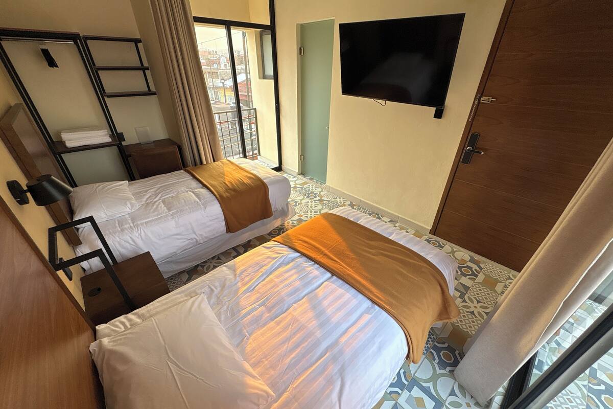 Habitación de hotel con dos camas, televisión, ventana con vistas y puerta.