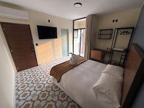 Une chambre d’hôtel avec un lit, un bureau, une chaise, une télévision et une fenêtre avec des rideaux.
