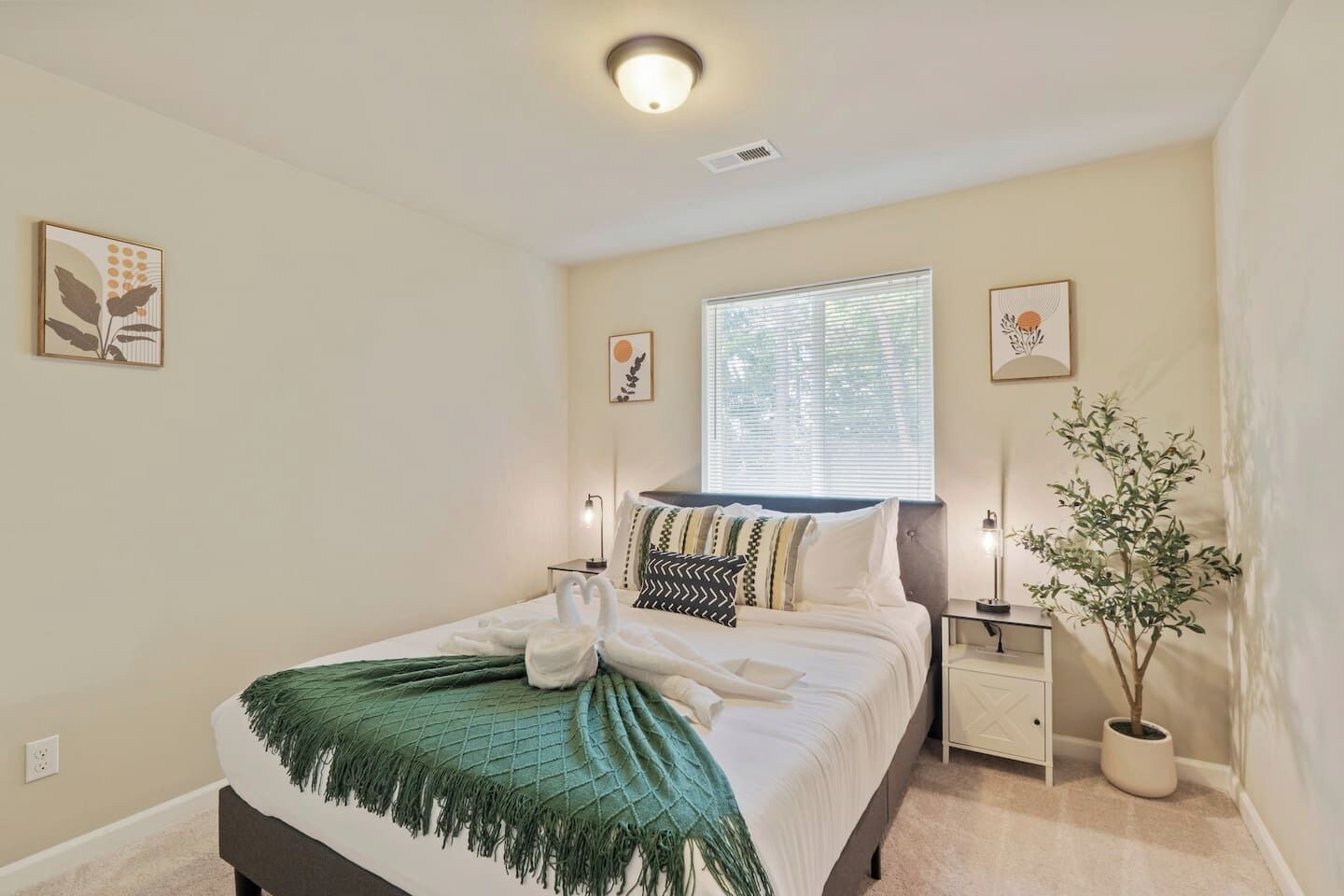 A bedroom with a bed, bedside tables, a window, and a potted plant.