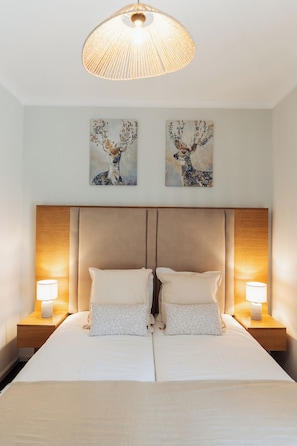 A double bed with two pillows, a headboard, bedside lamps, and two wall-mounted paintings of deer. - Views from the Villa_ Deluxe Double Room (12) w/ private bathroom (Cabeceiras de Basto) (Cabeceiras de Basto)
