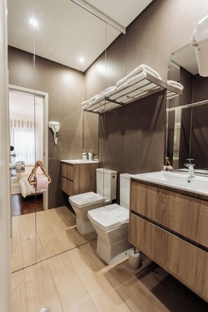Une salle de bain moderne avec une paroi de séparation en verre, un meuble-lavabo en bois, des toilettes blanches et un porte-serviettes.