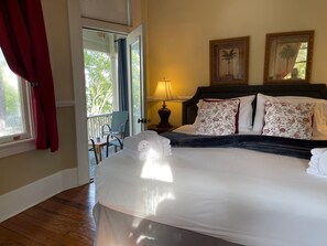 Ein Hotelzimmer mit Bett, Balkon, Stuhl und zwei gerahmten Bildern an der Wand.