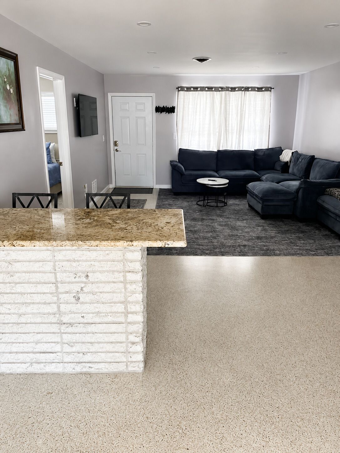 A modern living room with a dark sofa, a small round table, and a kitchen area with a white countertop.