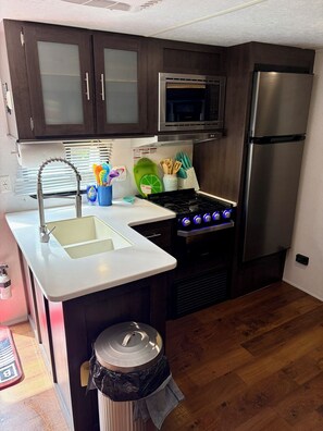 Eine kleine Küche mit Edelstahlkühlschrank, Mikrowelle, Gasherd und Holzschränken.