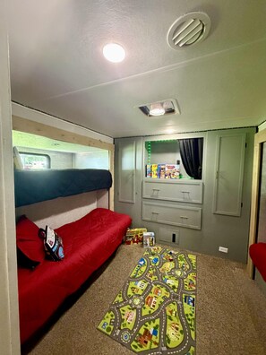 Ein kleines Zimmer mit Etagenbetten, einem Stauraum und einer Kinderspieledecke.