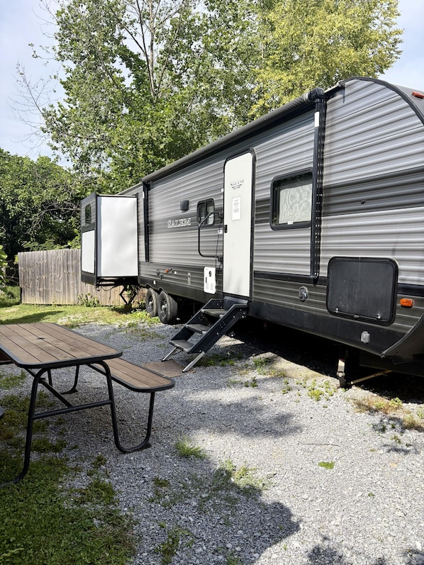 A recreational vehicle with a sliding door, a small window, and a step leading to the entrance. - 90's RV Rental - 90's Inspired Furnished RV Rental (Pigeon Forge)