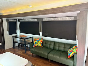 Ein Zimmer mit einem grünen Sofa, einem kleinen Tisch und zwei Fenstern mit Jalousien.
