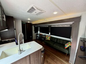 A compact living space with a kitchenette, a sofa, and a dining area. - 90's RV Rental - 90's Inspired Furnished RV Rental (Pigeon Forge)