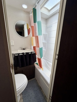 A bathroom with a toilet, sink, mirror, and shower. - 90's RV Rental - 90's Inspired Furnished RV Rental (Pigeon Forge)