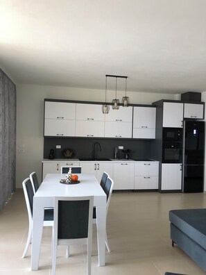 Eine moderne Küche mit weißen Schränken, einem schwarzen Kühlschrank und einem Essbereich mit weißem Tisch und Stühlen.