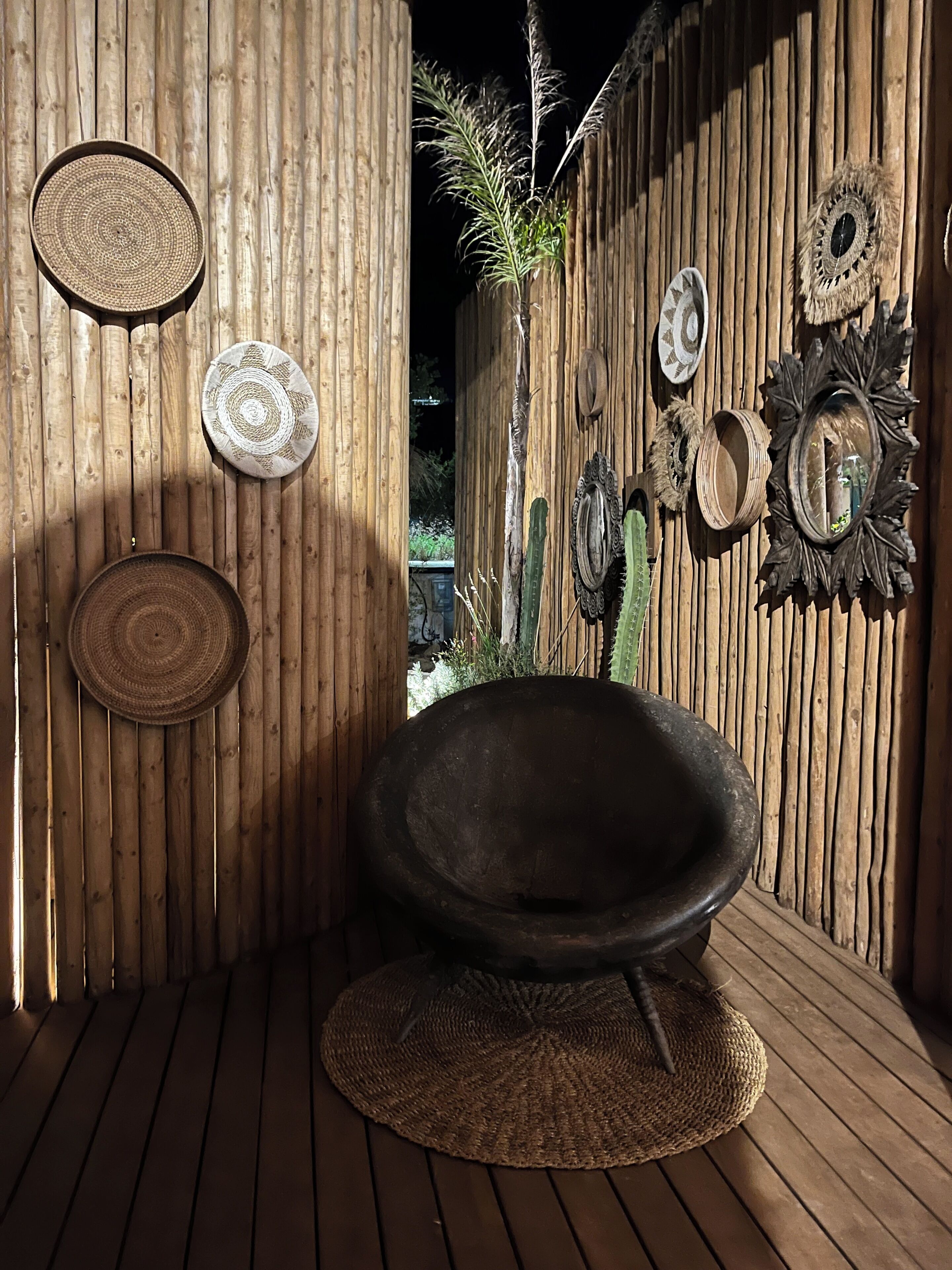 Une pièce au décor rustique, avec un tapis tissé, un grand saladier tissé et divers éléments décoratifs en tissu accrochés aux murs.